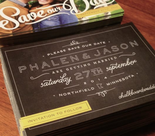 A pile of postcard sized 'save the date' mailers sitting on a tabletop.